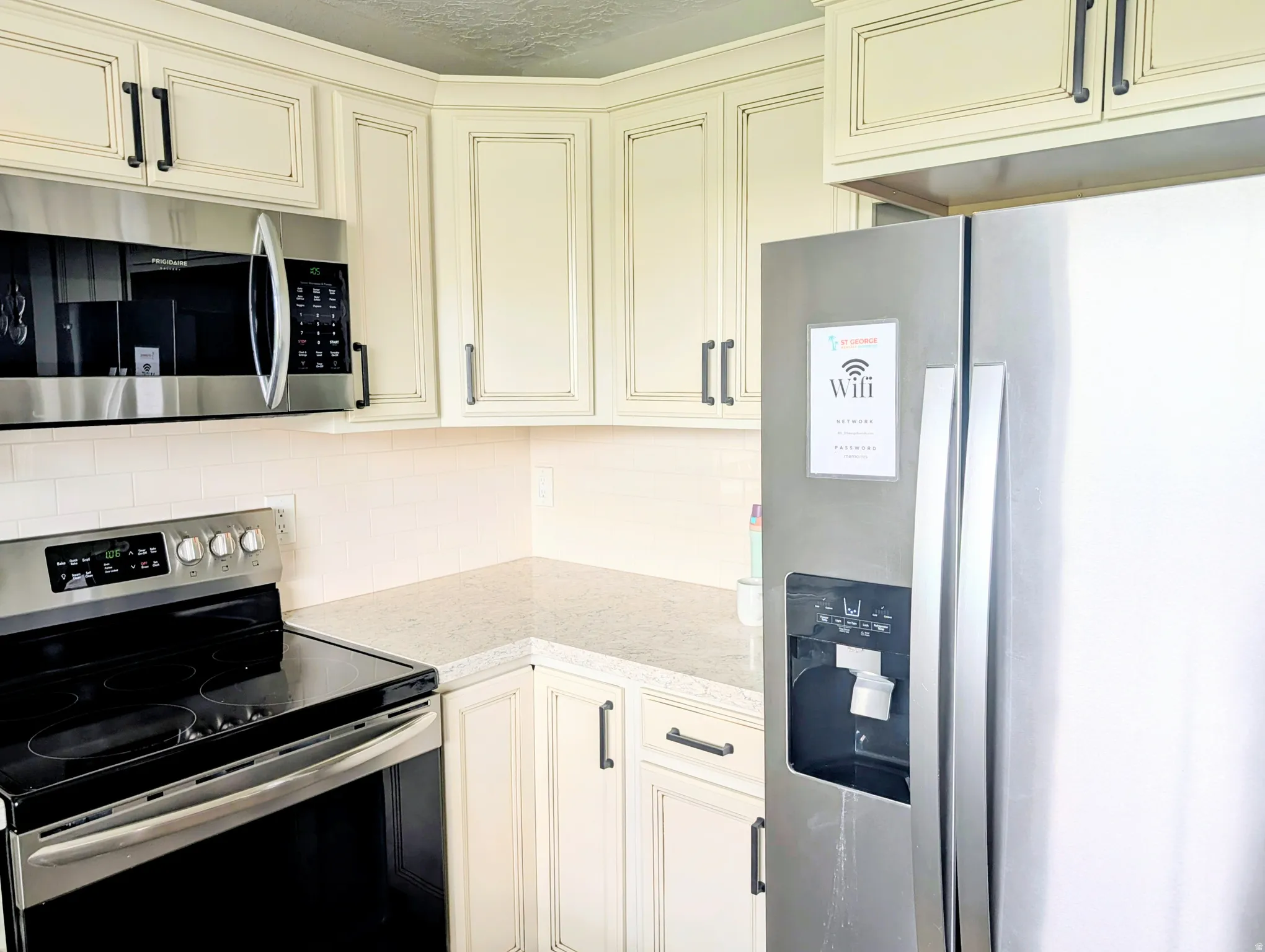 Updated kitchen featuring cream-finished cabinetry with brushed nickel hardware, stainless steel appliances including a French-door refrigerator and electric range, quartz countertops, and recessed ceiling lighting