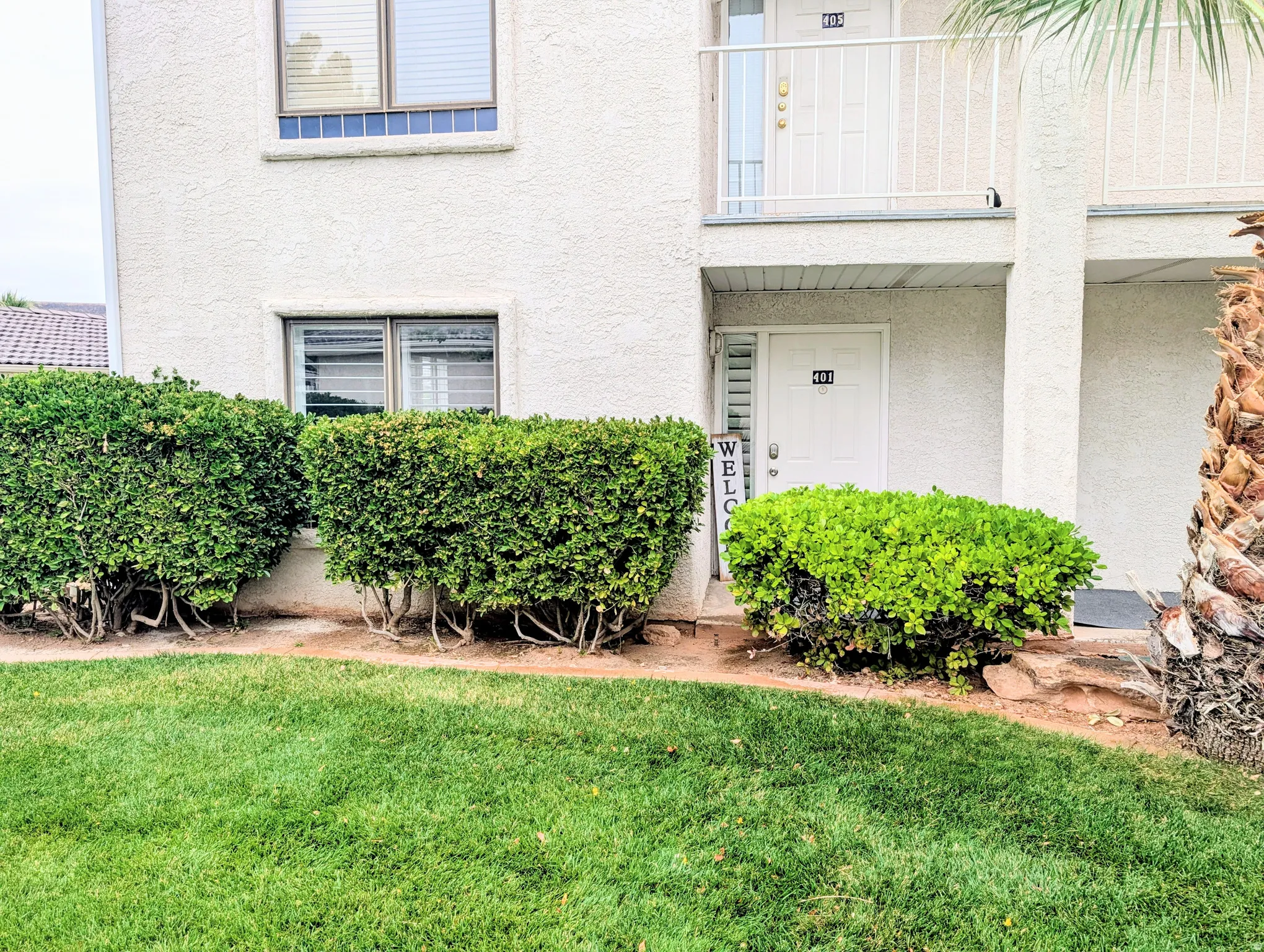 Stucco exterior with ground-level entry, first-story balcony, and mature shrubs