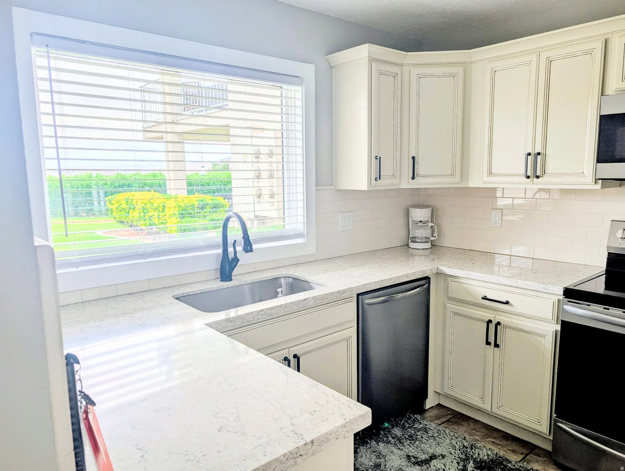 Bright, contemporary kitchen featuring cream-painted cabinetry with black hardware, white subway tile backsplash, and light stone countertops