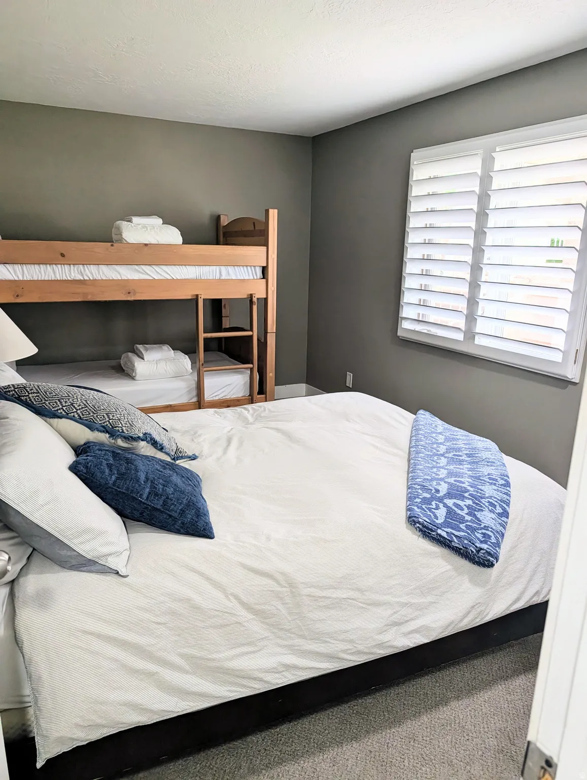 Carpeted room with a wooden bunk bed, a platform bed, and white window shutters
