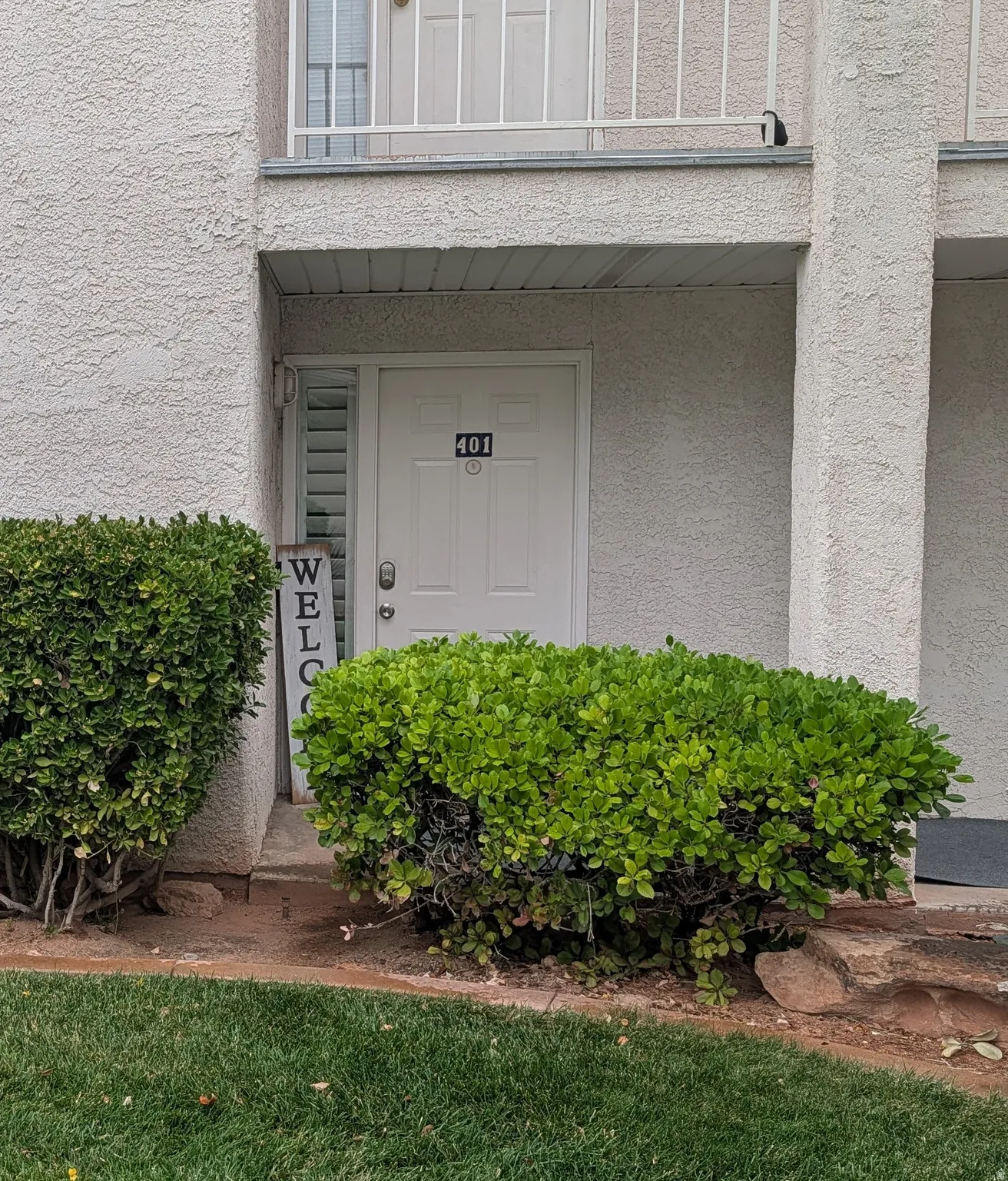 Stucco exterior with a covered entry, established foundational plantings, and a ground-level patio