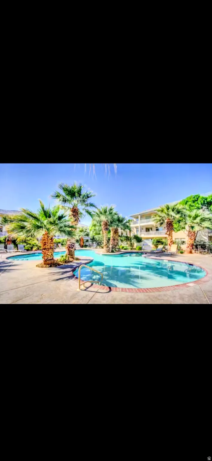 Resort-style pool area featuring multiple swimming pools, mature palm trees, concrete decking, and a surrounding building structure