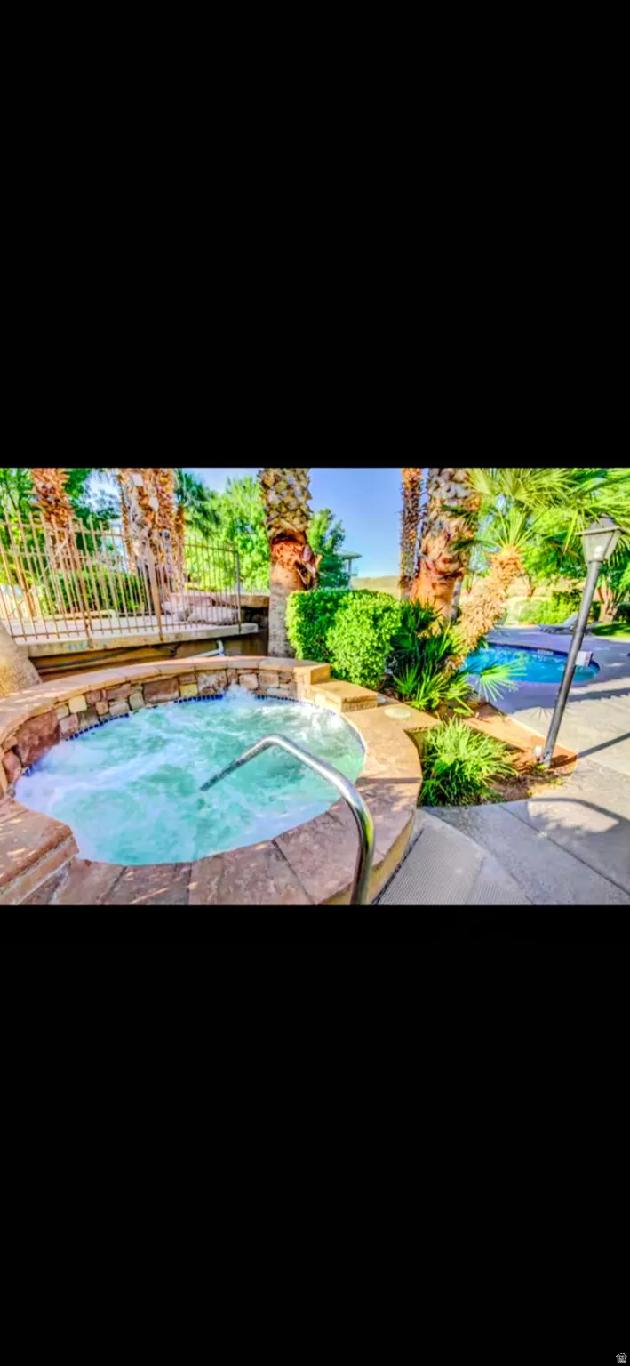 Stone-clad spa with bubbling water and a metal handrail, surrounded by tropical landscaping, integrated with a paved patio