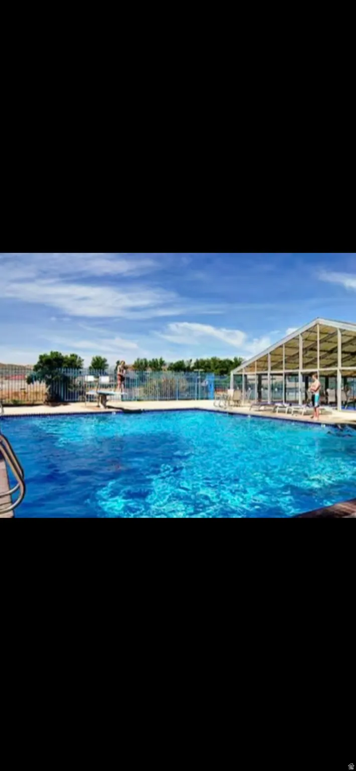 Outdoor swimming pool with a diving board, surrounding patio, and an adjacent structure featuring a gable roof and multiple windows