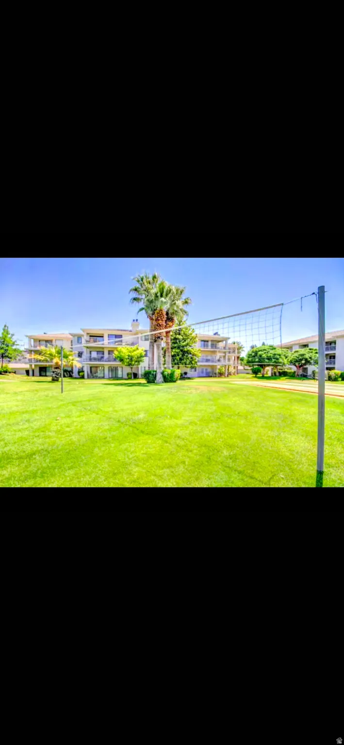 Expansive green space featuring a volleyball net, mature palm trees, and multi-story buildings with balconies