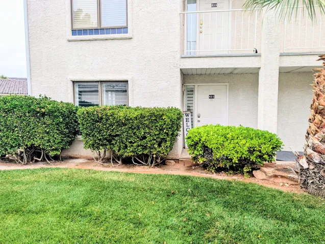 Stucco exterior with ground-level entry, first-story balcony, and mature shrubs