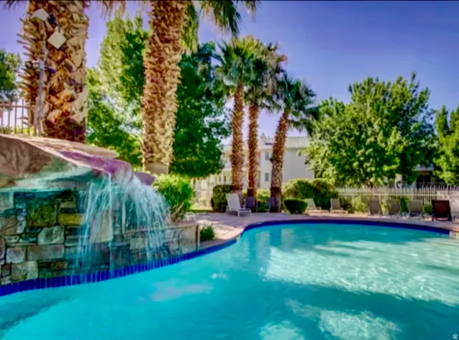 Resort-style pool featuring a rock waterfall, surrounding palm trees, and an adjacent deck area