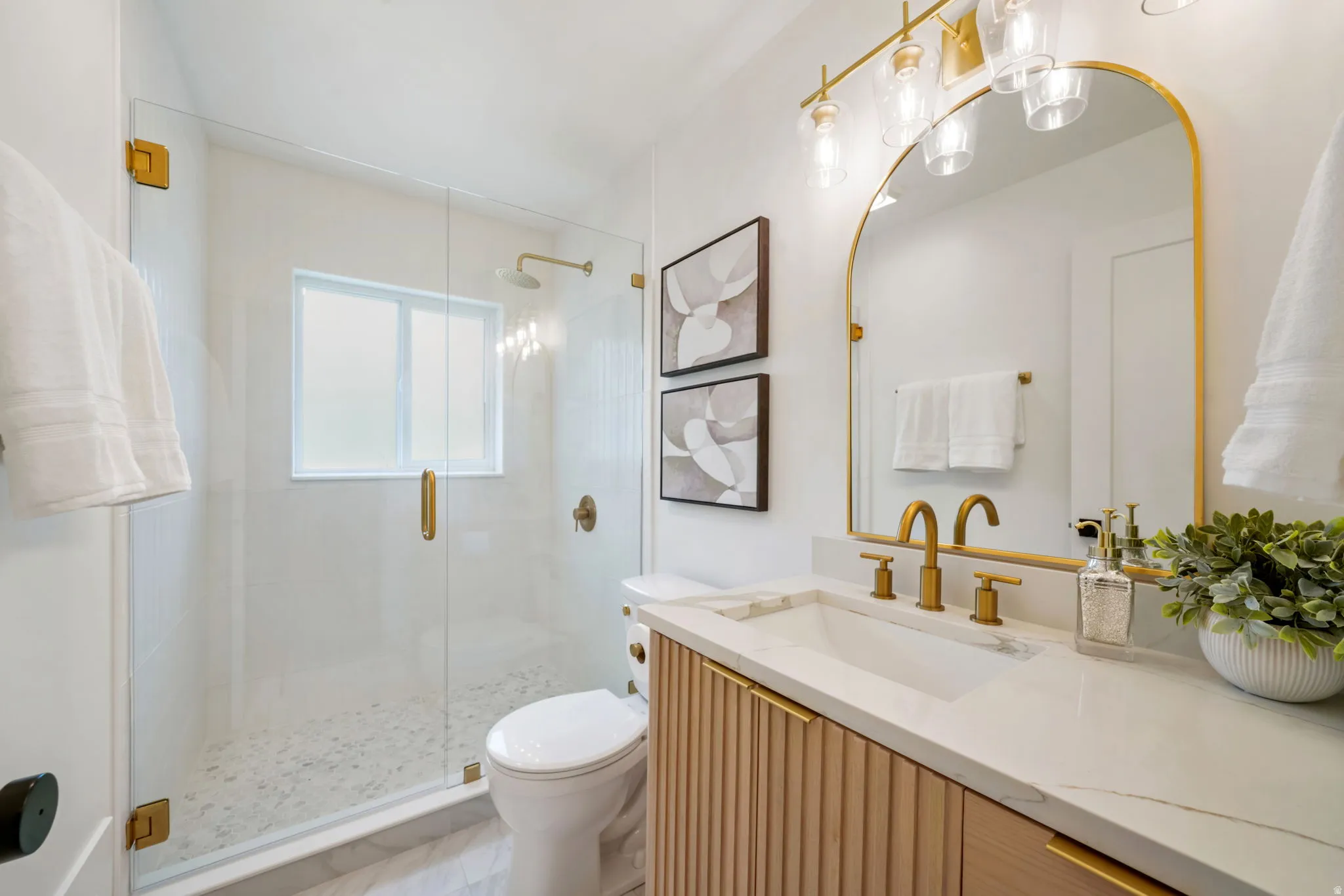 Glass-enclosed shower with a rainfall showerhead, a single vanity with a light wood-finish cabinet, a white stone countertop, and gold-finish fixtures