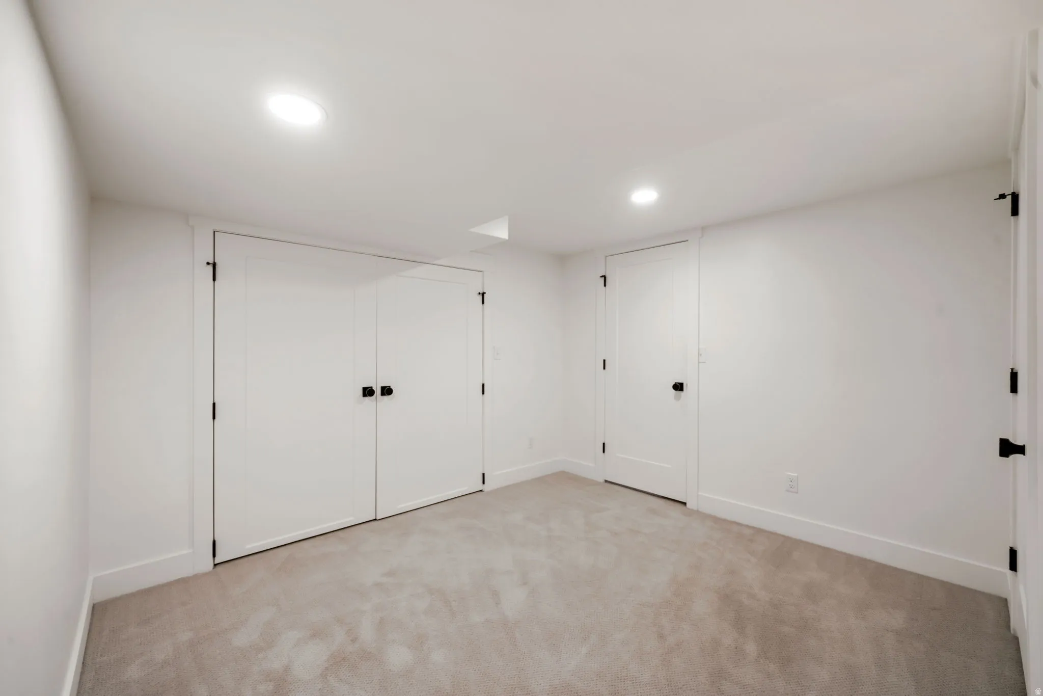 Recessed lighting illuminates a neutral carpeted room with white walls and trim