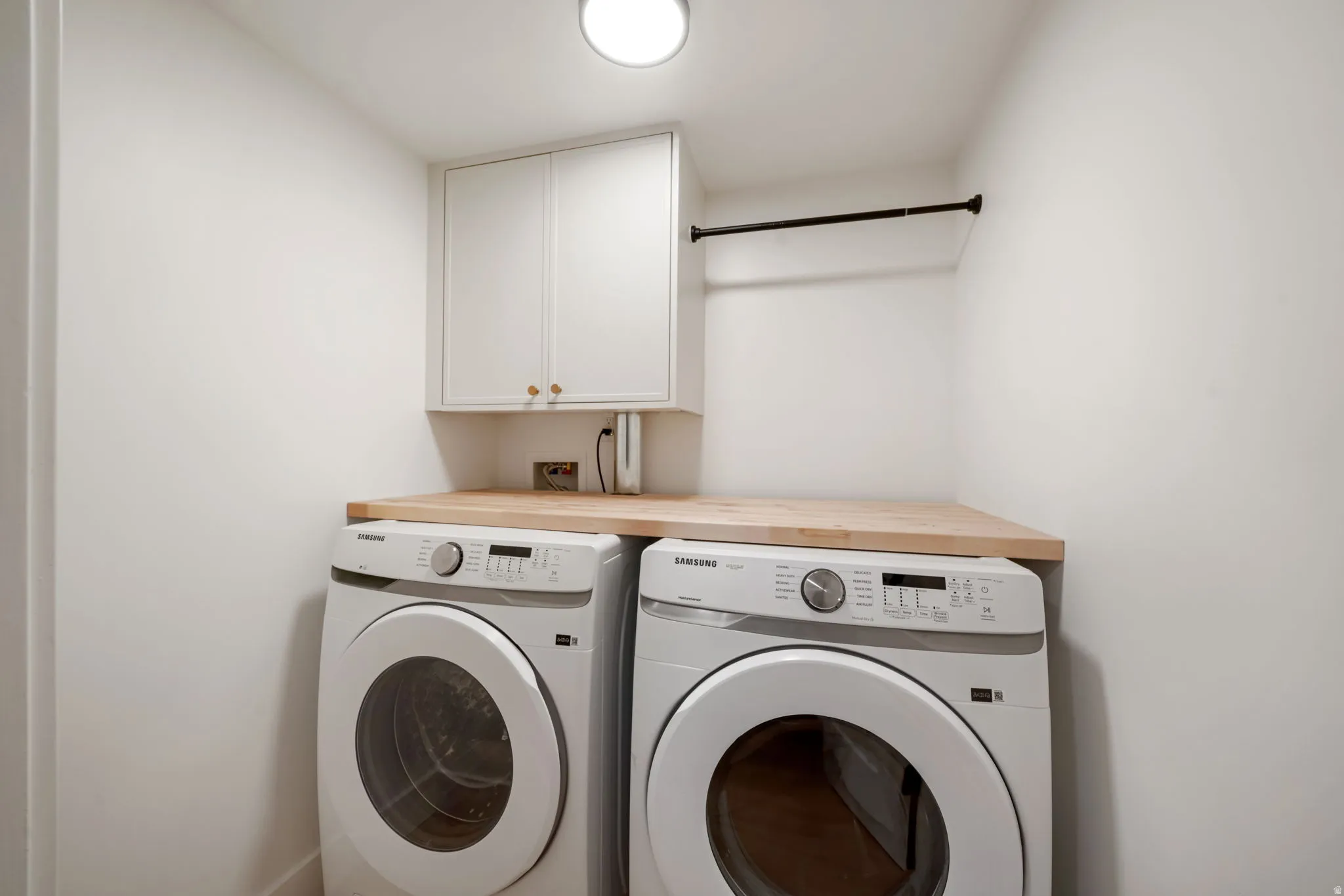 Compact laundry area featuring a wood-finish countertop, white cabinetry with brass-tone hardware, and a hanging rod