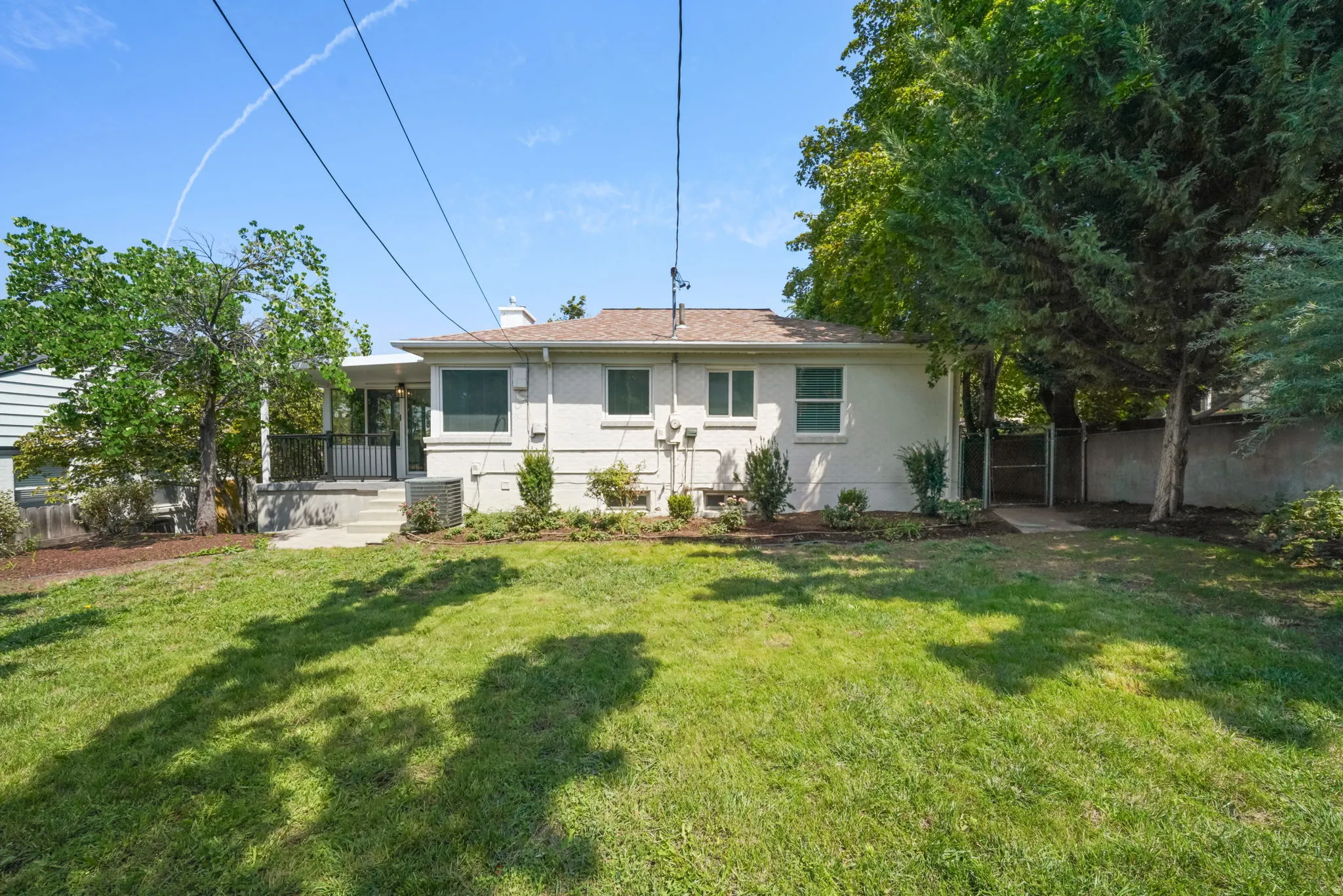 Classic white ranch home with a covered front porch, situated on a generous lawn bordered by mature shade trees