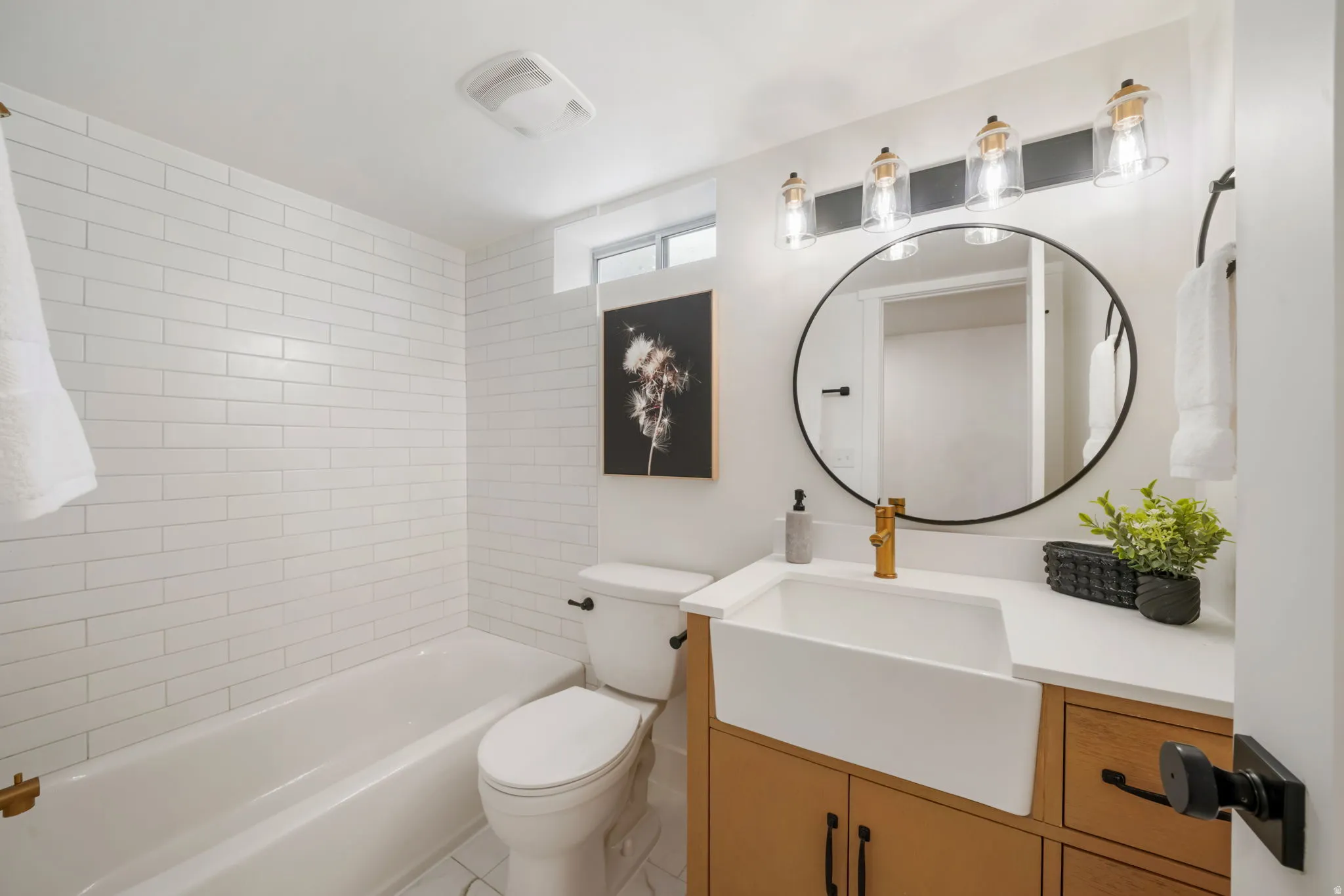 Modern bathroom featuring white subway tile surround, a wood-finish vanity with dual storage, a white rectangular vessel sink, and a circular black-framed mirror