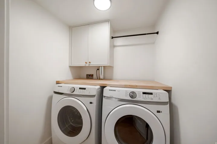 Compact laundry area featuring a wood-finish countertop, white cabinetry with brass-tone hardware, and a hanging rod
