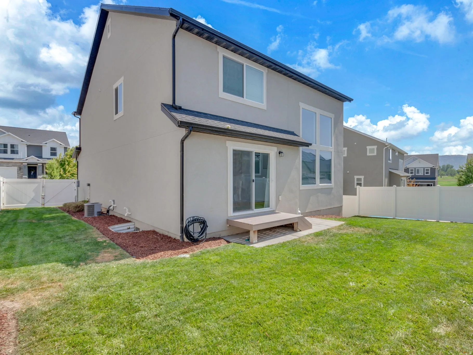 Expansive backyard featuring a manicured lawn, white vinyl fencing, and a ground-level deck with a sliding glass door
