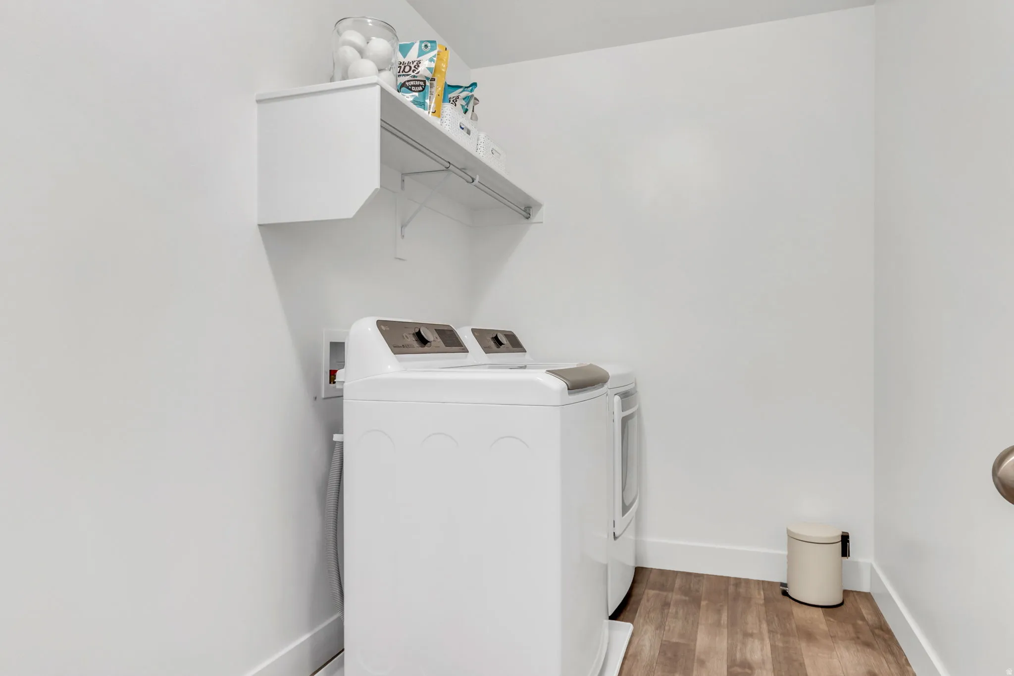 Dedicated laundry area featuring wood-finish flooring, white walls, and a wall-mounted storage shelf