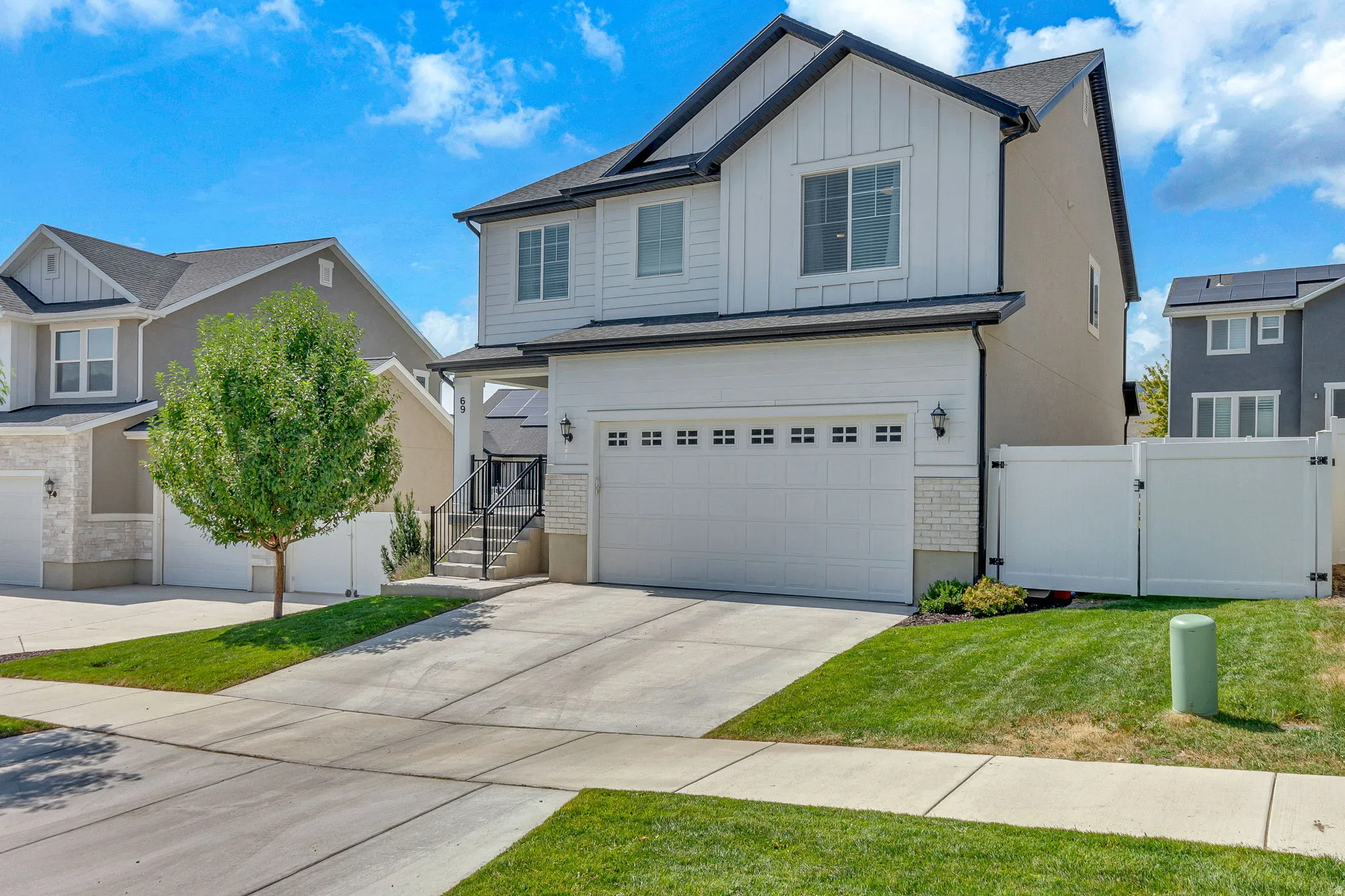 Modern two-story residence featuring a two-car garage, white vertical siding, dark trim accents, a concrete driveway, and a white privacy fence