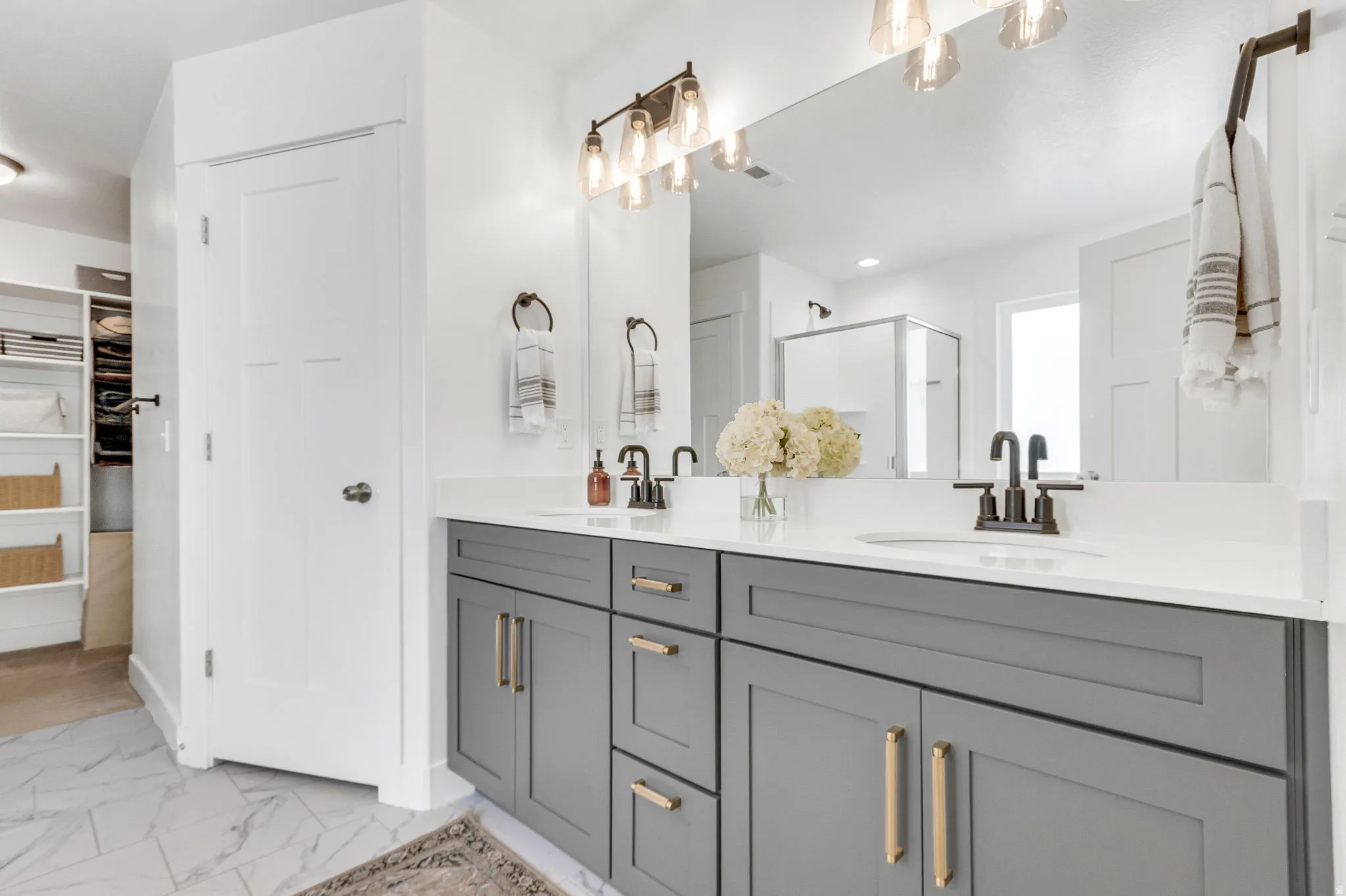 Dual vanity with gray cabinetry, brushed gold hardware, and white countertops