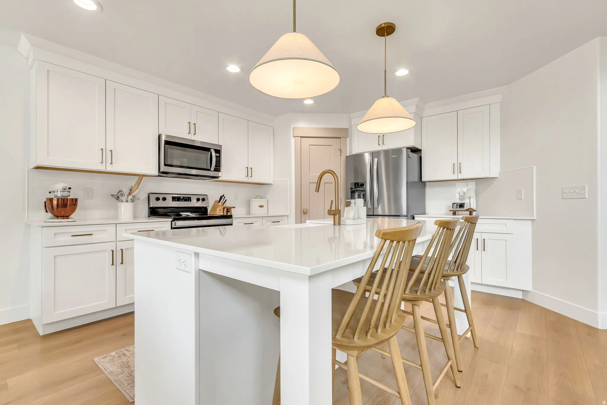 Bright kitchen featuring white shaker cabinetry, stainless steel appliances, a center island with countertop seating, recessed lighting, and wood-finish flooring