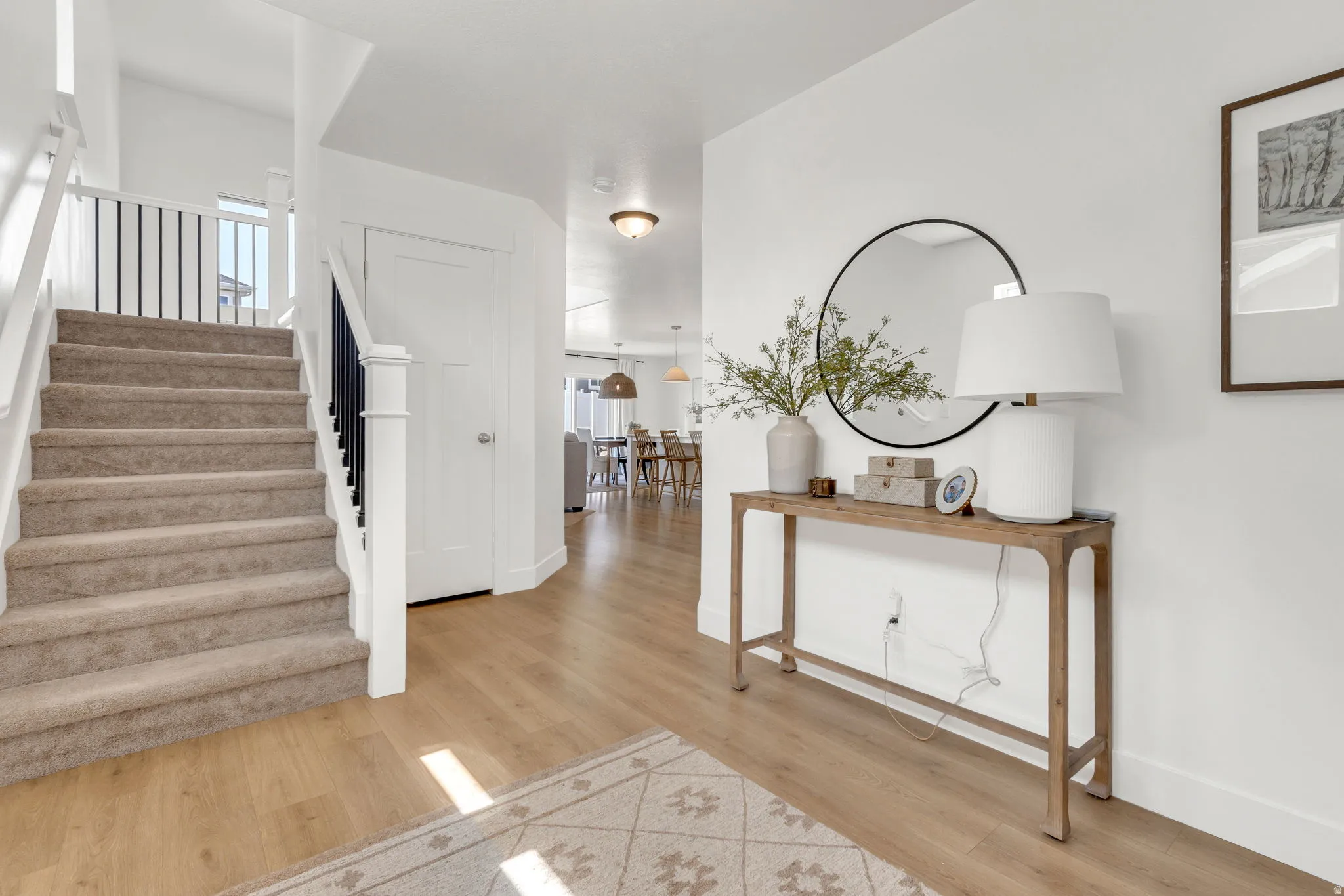 Bright entryway featuring wood-finish flooring, a carpeted staircase with white risers, and black iron balusters