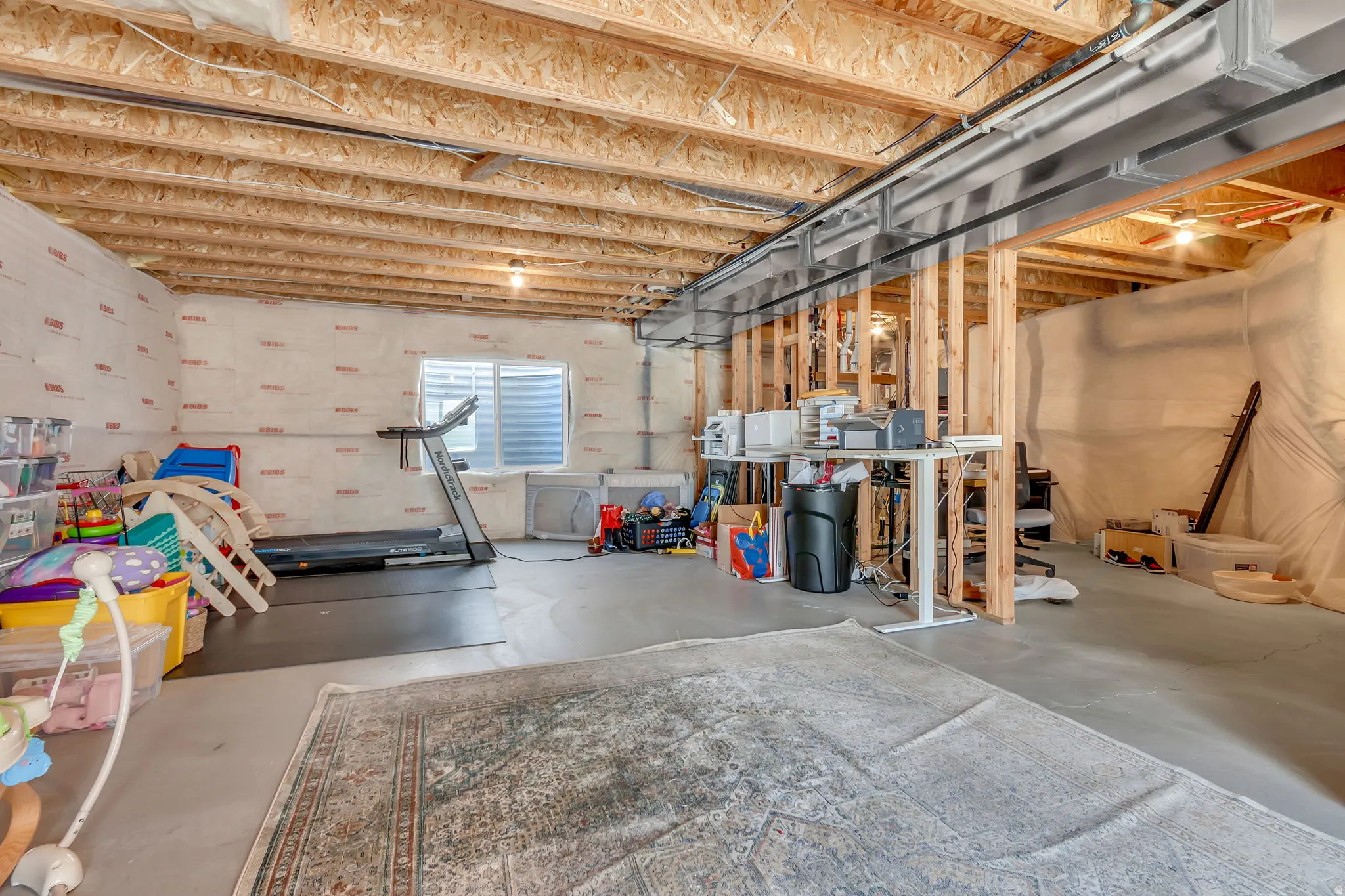 Unfinished basement featuring exposed wood joists, concrete flooring, and a small window with horizontal blinds
