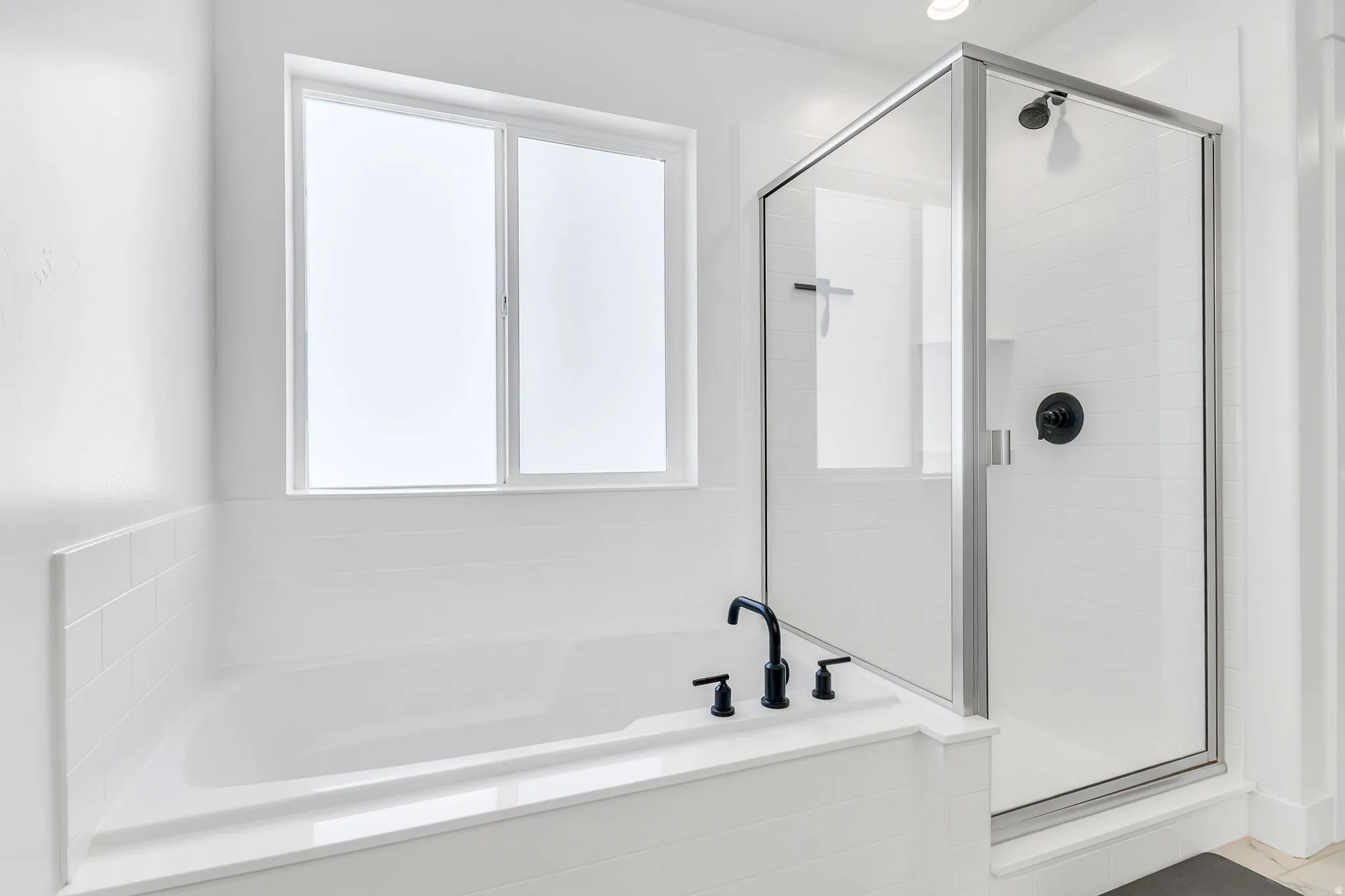 White subway tile tub surround with black fixtures and a glass-enclosed shower featuring a black shower head and handle