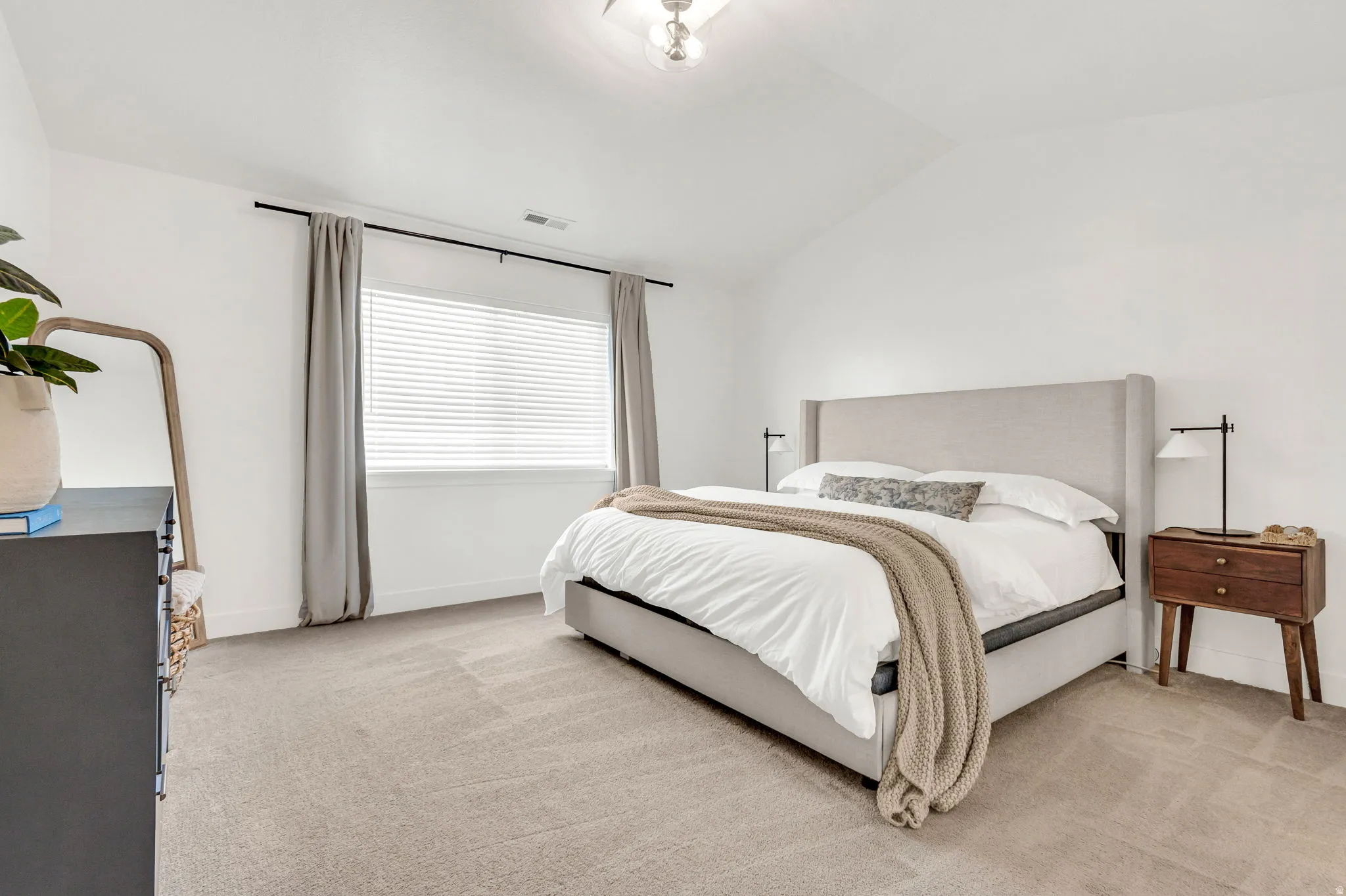Spacious room featuring vaulted ceilings, a large window with blinds, and light-toned carpeting