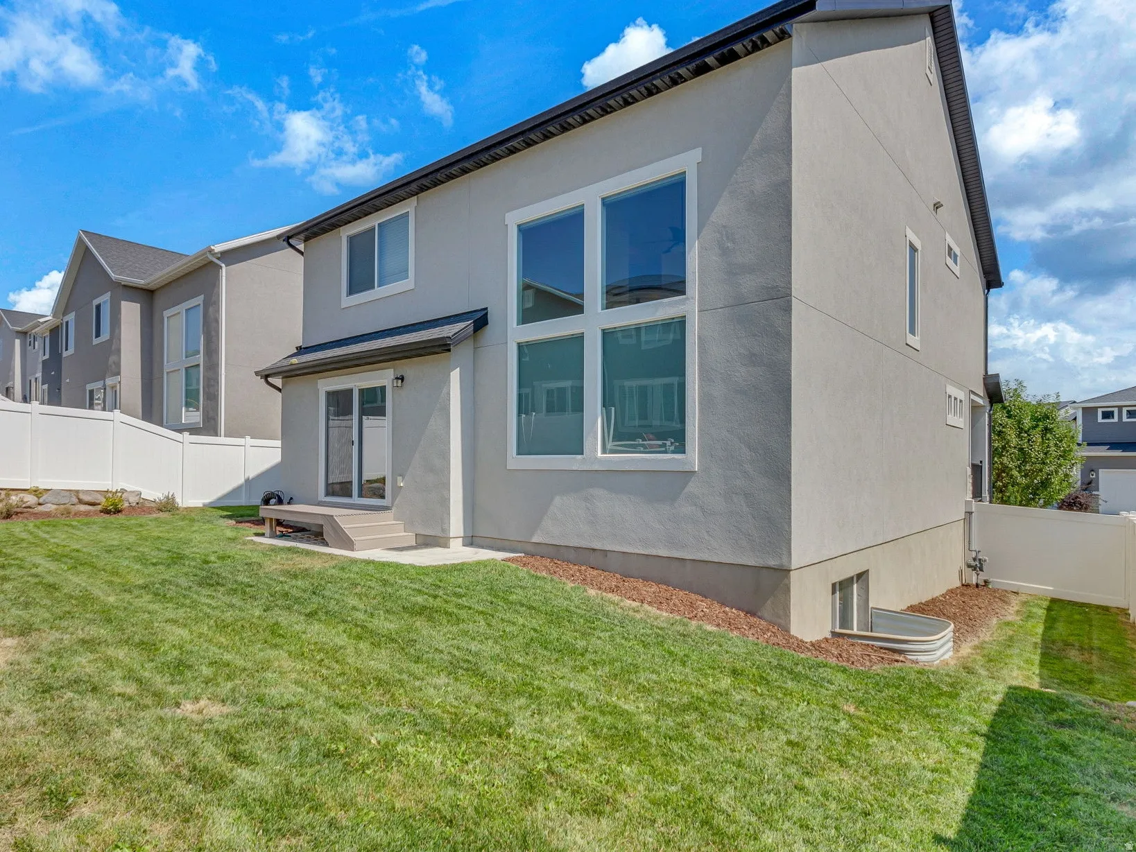 Rear exterior featuring a sliding glass door, a large picture window, and a white vinyl fence
