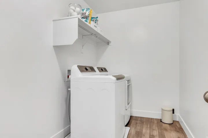 Dedicated laundry area featuring wood-finish flooring, white walls, and a wall-mounted storage shelf