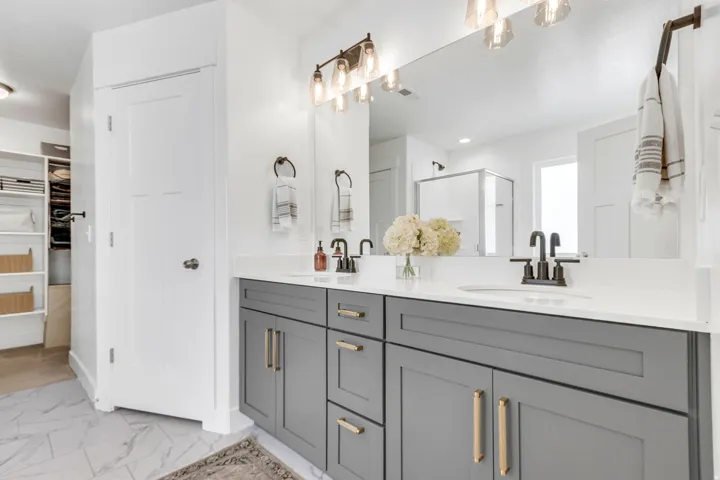 Dual vanity with gray cabinetry, brushed gold hardware, and white countertops