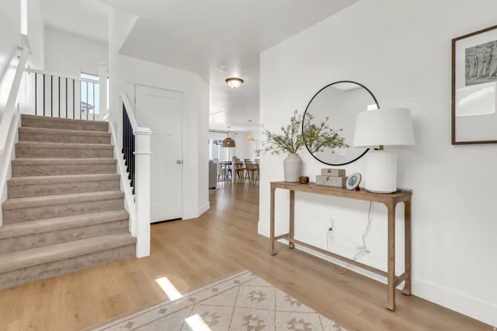 Bright entryway featuring wood-finish flooring, a carpeted staircase with white risers, and black iron balusters