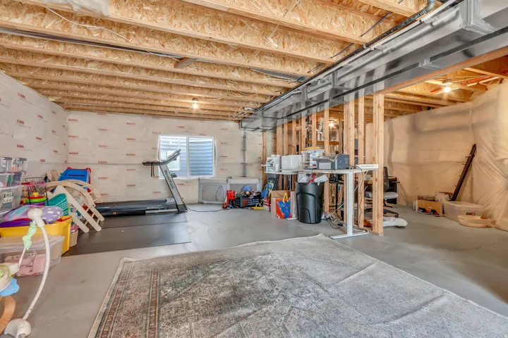 Unfinished basement featuring exposed wood joists, concrete flooring, and a small window with horizontal blinds