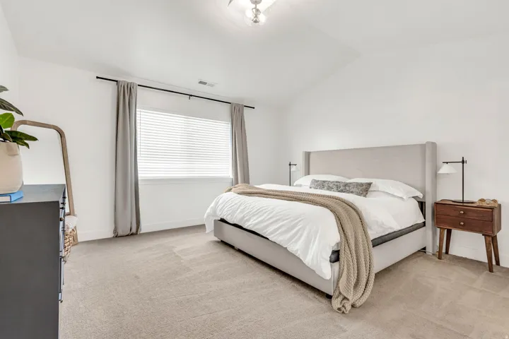 Spacious room featuring vaulted ceilings, a large window with blinds, and light-toned carpeting