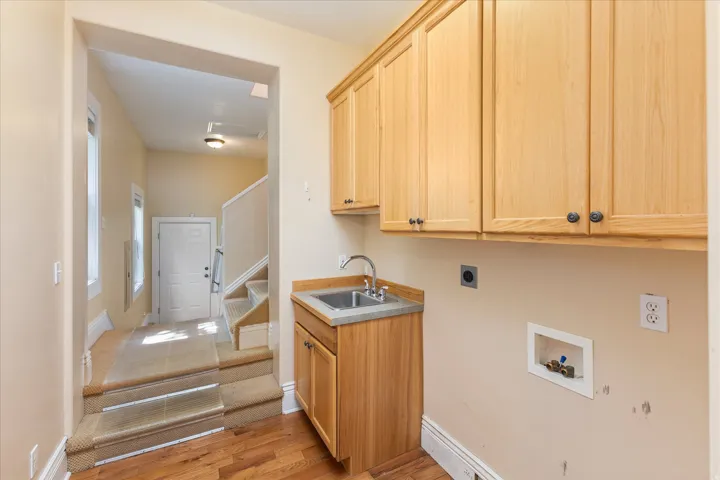 Utility area featuring wood-finish flooring and light wood cabinetry with dark hardware