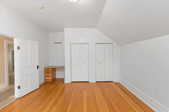 Spacious bedroom featuring hardwood flooring, multiple closets with white bi-fold doors, sloped ceilings, and abundant natural light