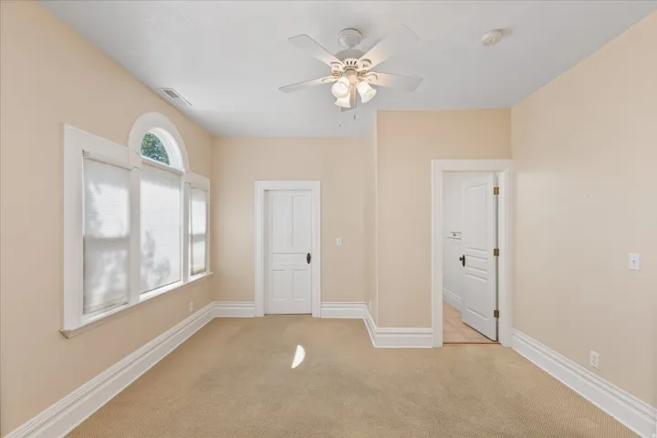 Room featuring a multi-pane window with an arched transom, a ceiling fan with integrated lighting, and multiple paneled doors