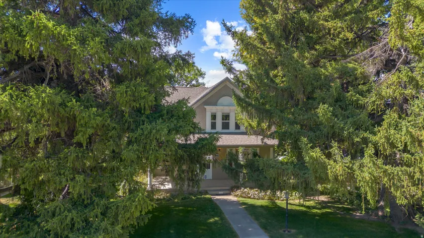 Traditional-style residence featuring a prominent arched window, multi-pane windows, a covered front porch, and mature evergreen trees framing the property