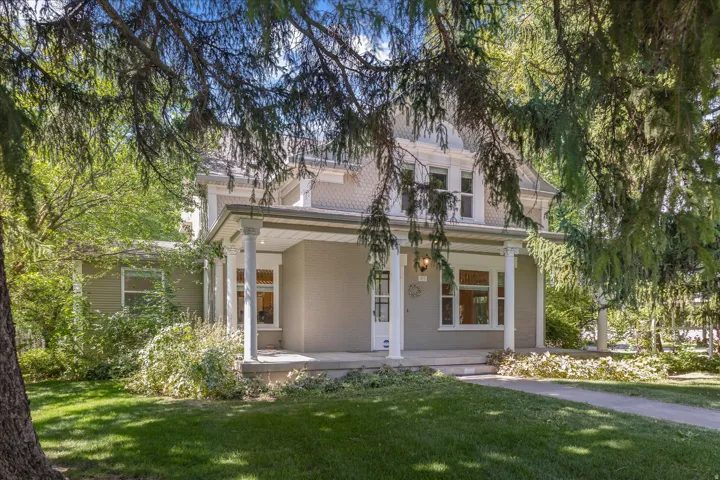 Two-story property featuring a covered front porch with white columns, a manicured lawn, and mature trees providing natural shading