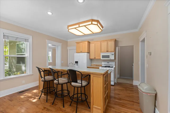 Kitchen featuring a central island with countertop seating, light wood cabinetry, white appliances, wood-finish flooring, and crown molding