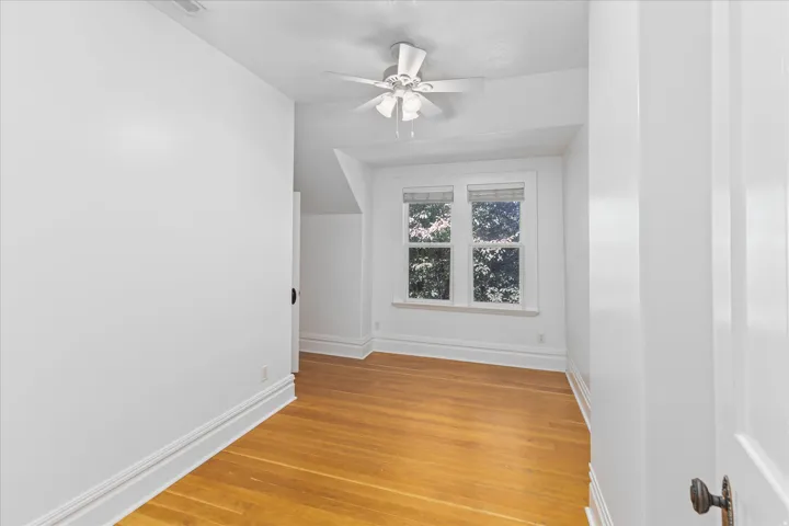 Room featuring wood-finish flooring, white trim, a ceiling fan, and two windows