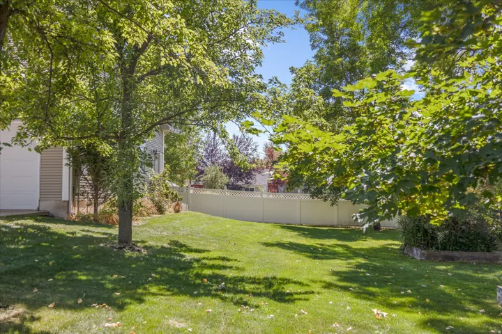 Expansive lawn area featuring mature trees, a white privacy fence, and a neutral-toned siding exterior