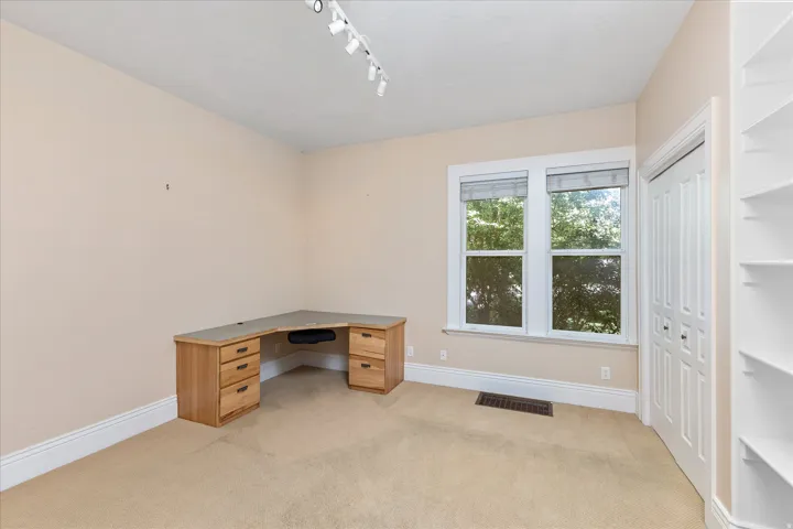 Carpeted room featuring a double window, built-in shelving, track lighting, and a bi-fold closet
