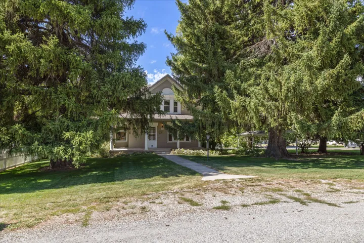 Fenced front yard with mature evergreen trees, manicured lawn, and a concrete pathway leading to a covered porch entry