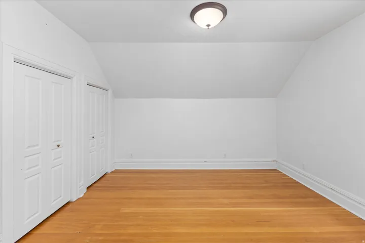 Room featuring wood flooring, white walls, and a sloped ceiling