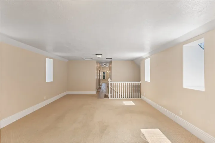 Expansive carpeted room featuring a white balustrade, multiple windows for natural light, recessed lighting, and crown molding