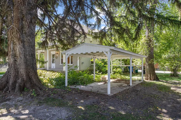 Property exterior featuring a carport with a concrete pad, mature trees, and a covered front porch with white columns