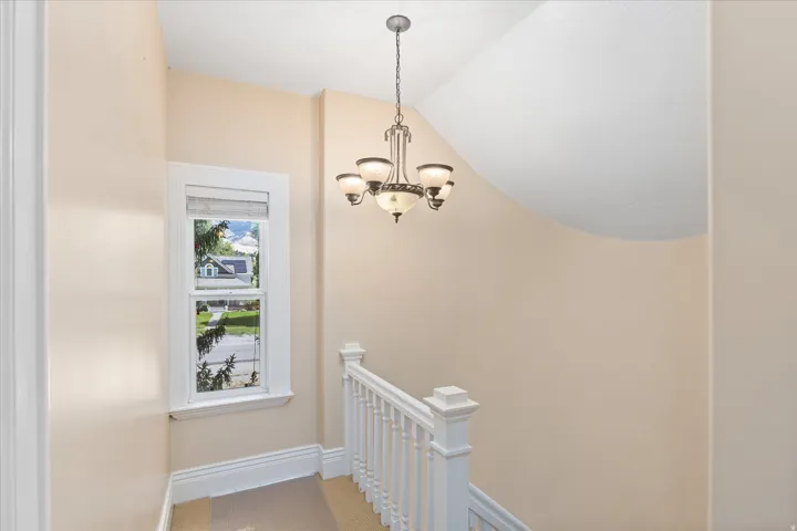 Stairwell featuring a traditional chandelier, white baluster railing, and a window with white trim