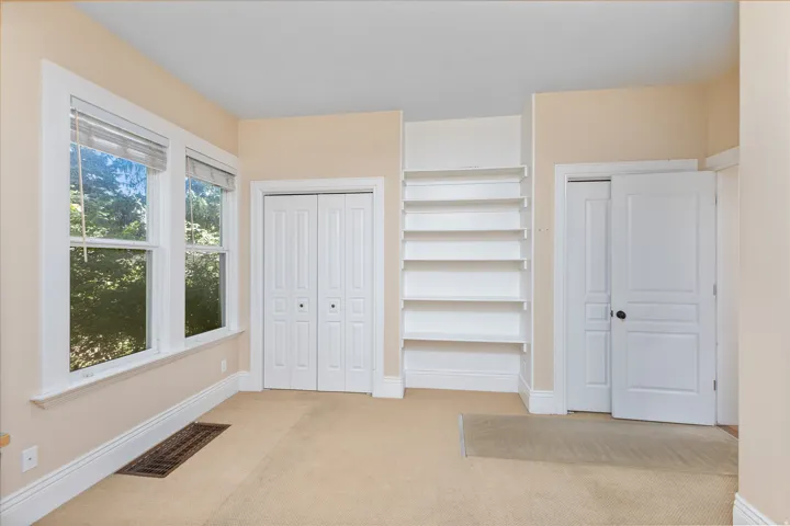 Room featuring twin windows, built-in shelving, two bifold closet doors, and an additional solid panel door
