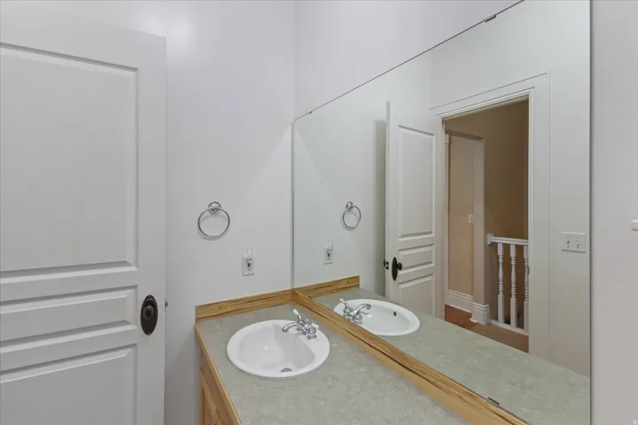 Bathroom vanity featuring a light-toned countertop with integrated white oval sinks, a full-width mirror, and a wood-finish base cabinet