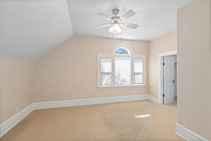 Carpeted room featuring a ceiling fan, arched transom window, white trim, and a paneled interior door