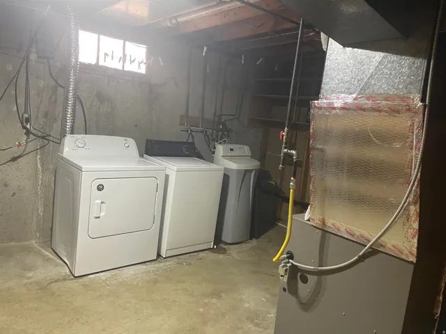 Dedicated laundry area featuring a white dryer, matching washing machine, and water softener system